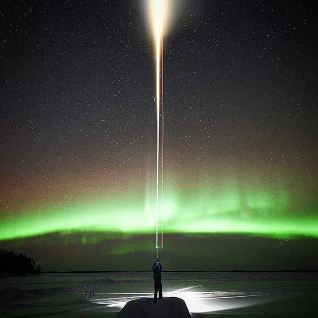 Aurora borealis over the frozen lake with a person shining a light skyward